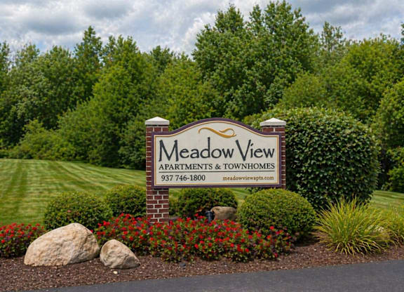 A sign for Meadow View Apartments and Townhomes is displayed in front of a green landscape.
