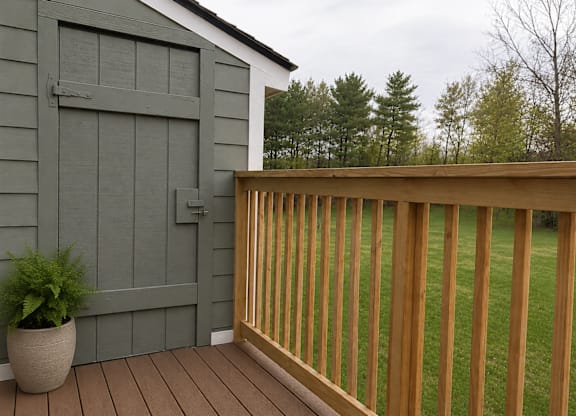 A wooden deck with a grey building and a potted plant.