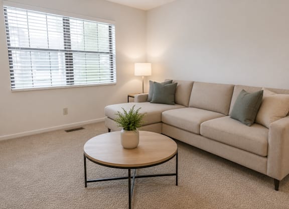 A living room with a beige couch, a round table, and a potted plant.