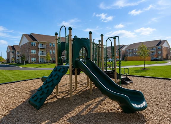 A green slide in a playground with a residential area in the background.