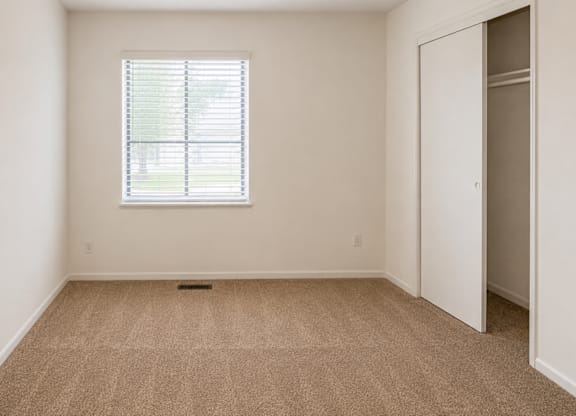 A room with a carpeted floor and a window with blinds.