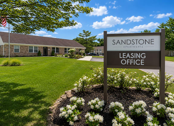A sign for the Sandstone Apartments leasing office stands in front of a building.