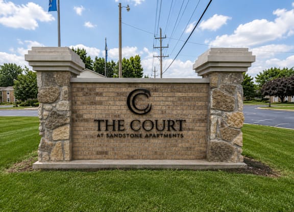 A sign for The Court at Sandstone Apartments is displayed in front of a grassy area.