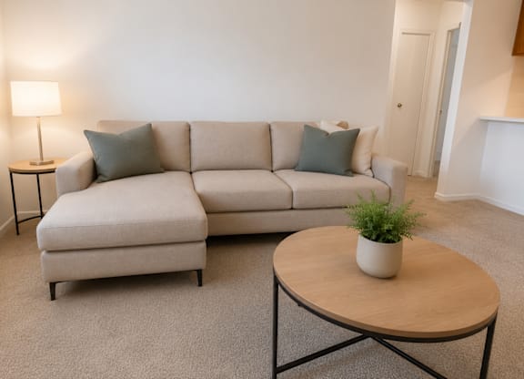 A living room with a beige couch, a small table with a plant on it, and a lamp on a side table.