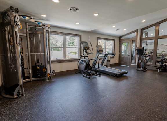a gym with treadmills and other fitness equipment in a home with windows