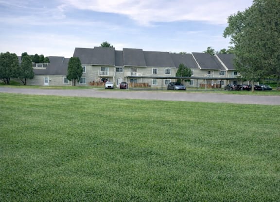A grassy field in front of a building with cars parked in the driveway.