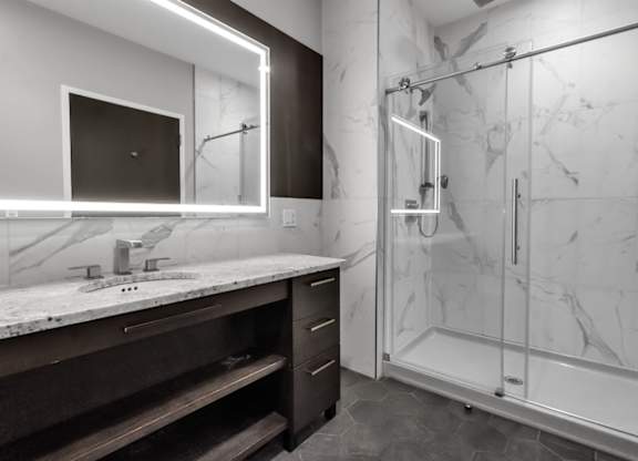 A modern bathroom with a walk-in shower and a vanity with a marble countertop.