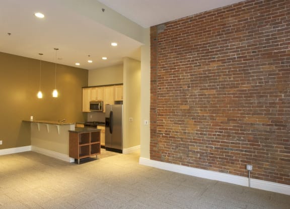 an empty living room with a brick wall and a kitchen at The Granite Works Apartments , New York 14202