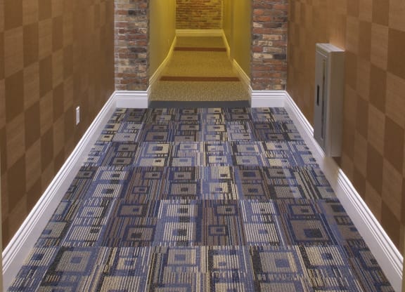 a hallway with a carpeted floor and a brick wall with a ceiling light at The Granite Works Apartments , Buffalo, New York