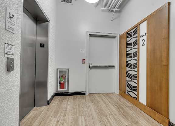 a hallway with a door to a elevator and a wood floor at 100 South Apartments, Buffalo, NY