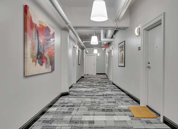 a long corridor with white walls and white doors and paintings at 100 South Apartments, Buffalo