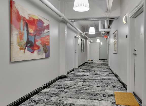 a long hallway with a painting on the wall and a rug on the floor at 100 South Apartments, Buffalo, NY 14202