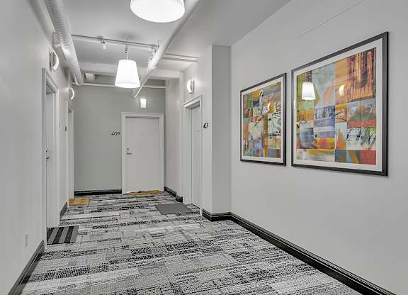 a long hallway with paintings on the wall and a door at the end of it at 100 South Apartments, Buffalo, NY