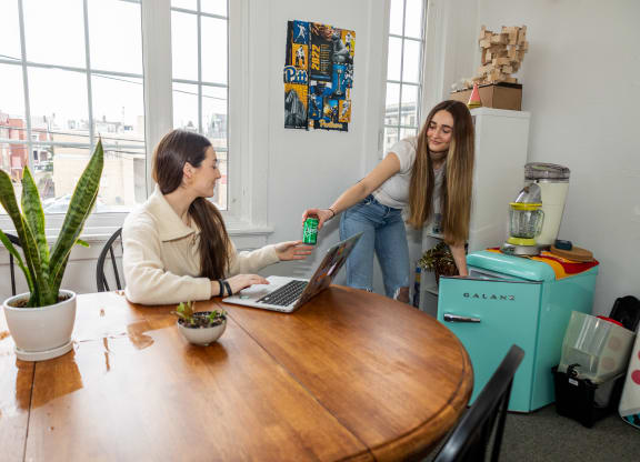 two women sit at a table with a laptop and a coffee pot at University Commons Apartments, Oakland, Pittsburgh
