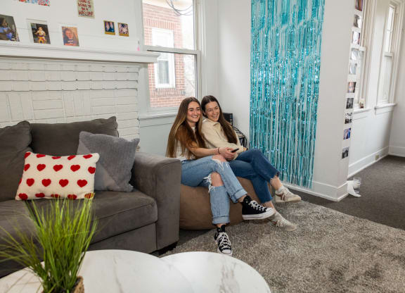 two girls sitting on a couch in a living room at University Commons Apartments, Oakland, Pittsburgh