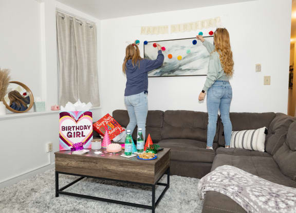 two girls hanging a happy birthday banner on a wall in a living room at University Commons Apartments, Oakland, Pittsburgh