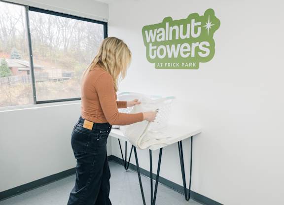 A woman is setting up a table in a room with a sign at Walnut Towers at Frick Park, Pittsburgh, 15217