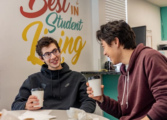 two students sitting at a table in front of a sign that says best in student living at University Commons Apartments, Oakland, Pittsburgh