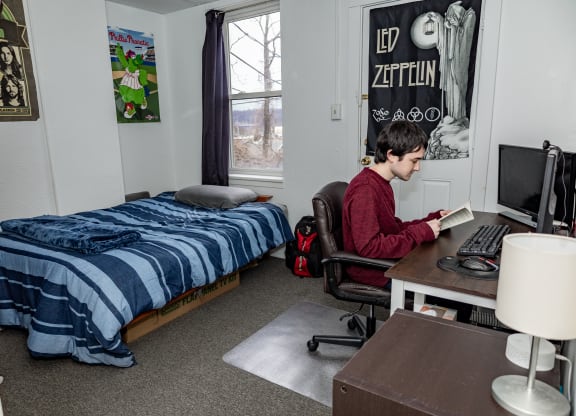 a student sits at a desk in a dorm room with a bed in the background at University Commons Apartments, Oakland, Pittsburgh