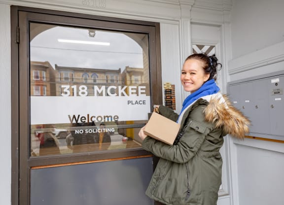 a woman standing in front of a door with a cardboard box in her hand at University Commons Apartments, Oakland, Pittsburgh