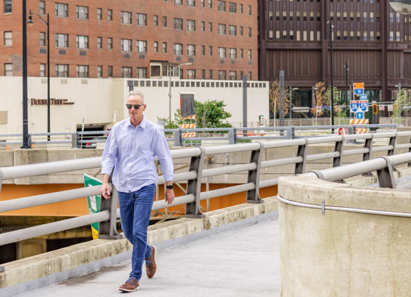 a man in a blue shirt and jeans walking across a bridge at The Washington at Chatham, Pittsburgh, PA 15219