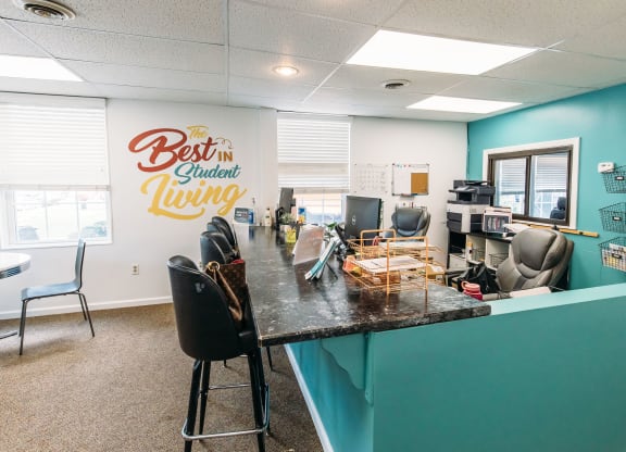 a desk with chairs and a counter in front of a wall with a sign that says best at University Commons Apartments, Oakland, Pittsburgh