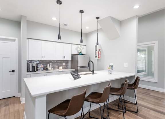 A kitchen with white countertops and brown chairs.