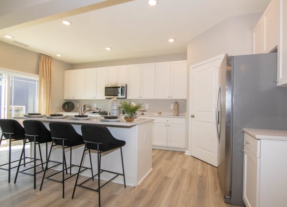 a kitchen with white cabinets and a counter with three stools at Jackson Run Townhomes, Whitestown, IN