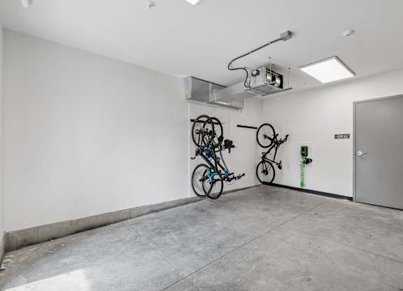 A room with a white wall and a grey door has a bicycle hanging on the wall.