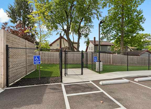 A parking lot with a black fence and a blue sign with a white wheelchair symbol.