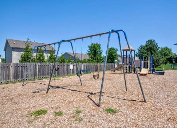 A playground with a blue swing set and a wooden fence.