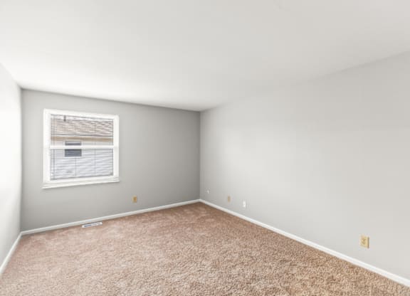 A room with a carpeted floor and a window with blinds.
