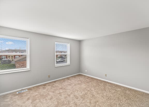 A room with a carpeted floor and a window showing a view of a residential area.