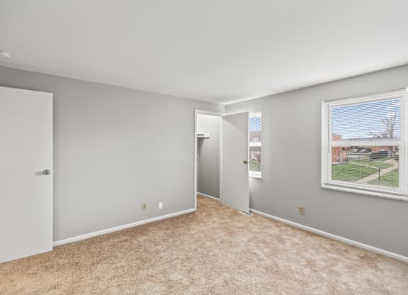 A room with carpeted floor and a window showing a view of a residential area.