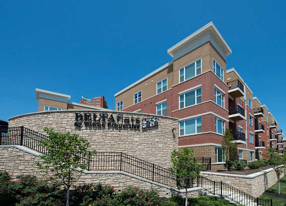 A multi-story residential building with a stone wall and a black metal railing.