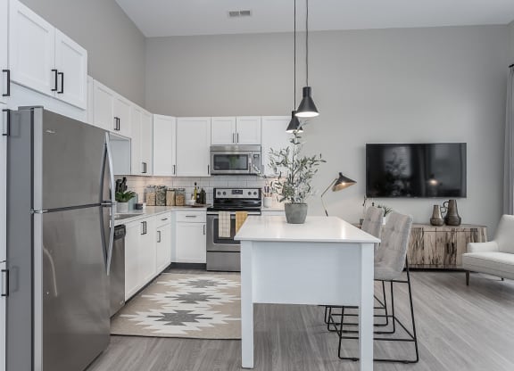 Liberty Township, OH, Apartments Near Paul Brown Stadium - Liberty Center - Modern Kitchen with Vinyl Wood Plank Flooring, Stainless Steel Appliances, White Quartz Countertops, White Cabinetry, Tile Backplash, Moveable Island with Grey Chairs, Pendant Lights, and Access to Living Room.