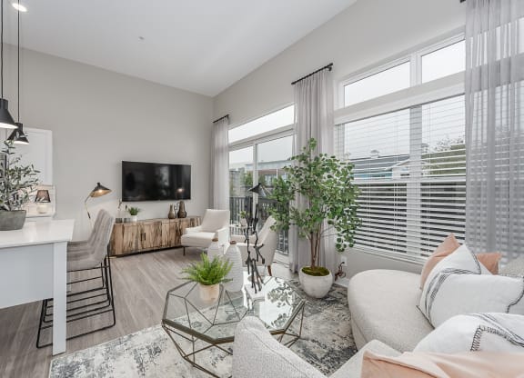 Apartments for Rent in West Chester OH - Liberty Center - Furnished Living Room with White Sofa, Glsas Coffee Table, Chairs, Wooden Storage Cabinet, Mounted TV, Large Windows, Decorative Plants, Pots,