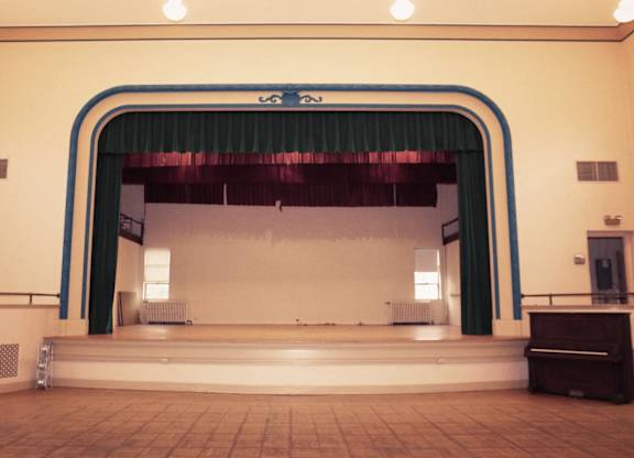 A stage with a green curtain and a piano on the floor.