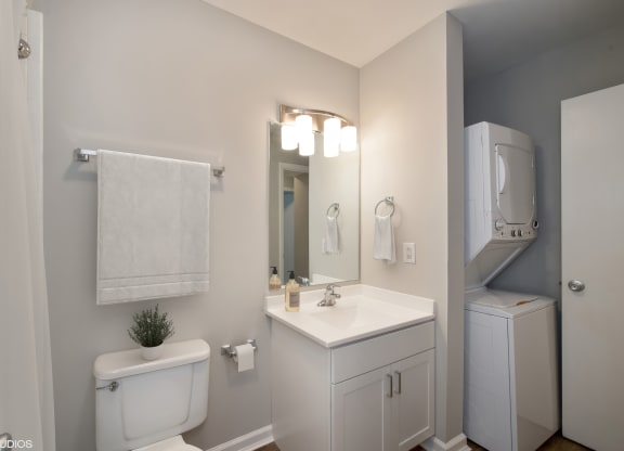 a bathroom with a toilet sink mirror and a washer and dryer at 7 Pointe Apartments, Indianapolis, 46205