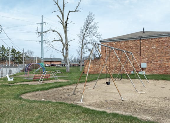A playground with swings and a slide in front of a brick building.