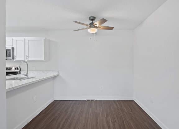 an empty living room with a ceiling fan and a kitchen