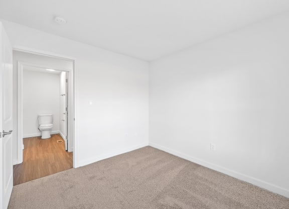 a bedroom with white walls and carpet and a bathroom with a toilet