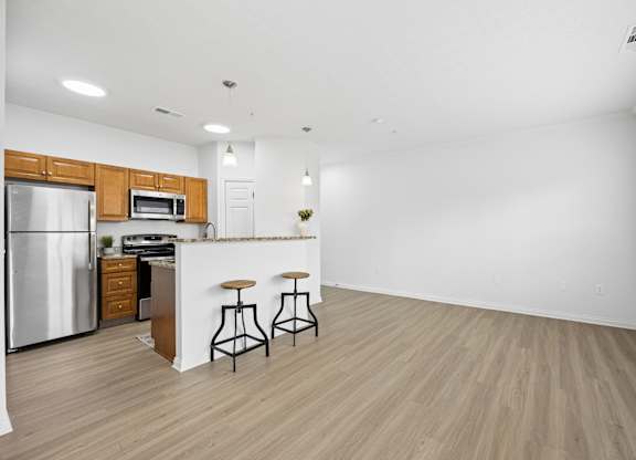 A kitchen with a refrigerator, microwave, and bar stools.