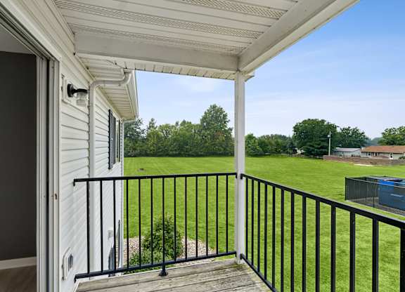 A balcony with a black railing and a view of a green lawn and trees.