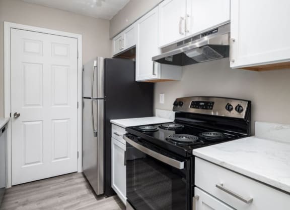 a kitchen with white cabinets and black appliances and a refrigerator at The Berryessa Apartments, Columbus, Ohio