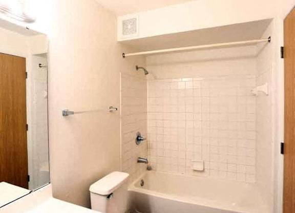 A white tiled bathroom with a toilet, sink, and bathtub.