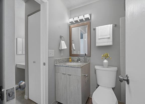 A white toilet is in a bathroom with a sink and mirror. at The Reserve at Grand Valley Apartments, Milford, OH