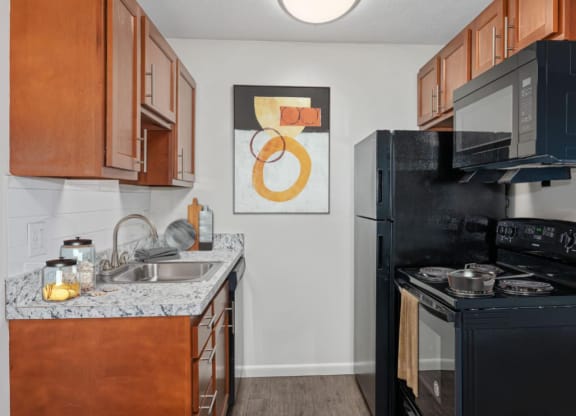 a kitchen with a black stove top oven next to a sink and a refrigerator at The Woodridge Collection, Ohio