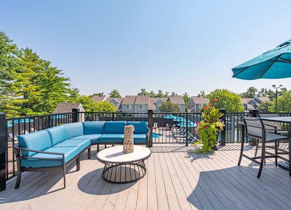 A blue sofa and a table with a vase of flowers are on a wooden deck.