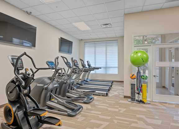 A gym with treadmills, exercise bikes, and a television.
